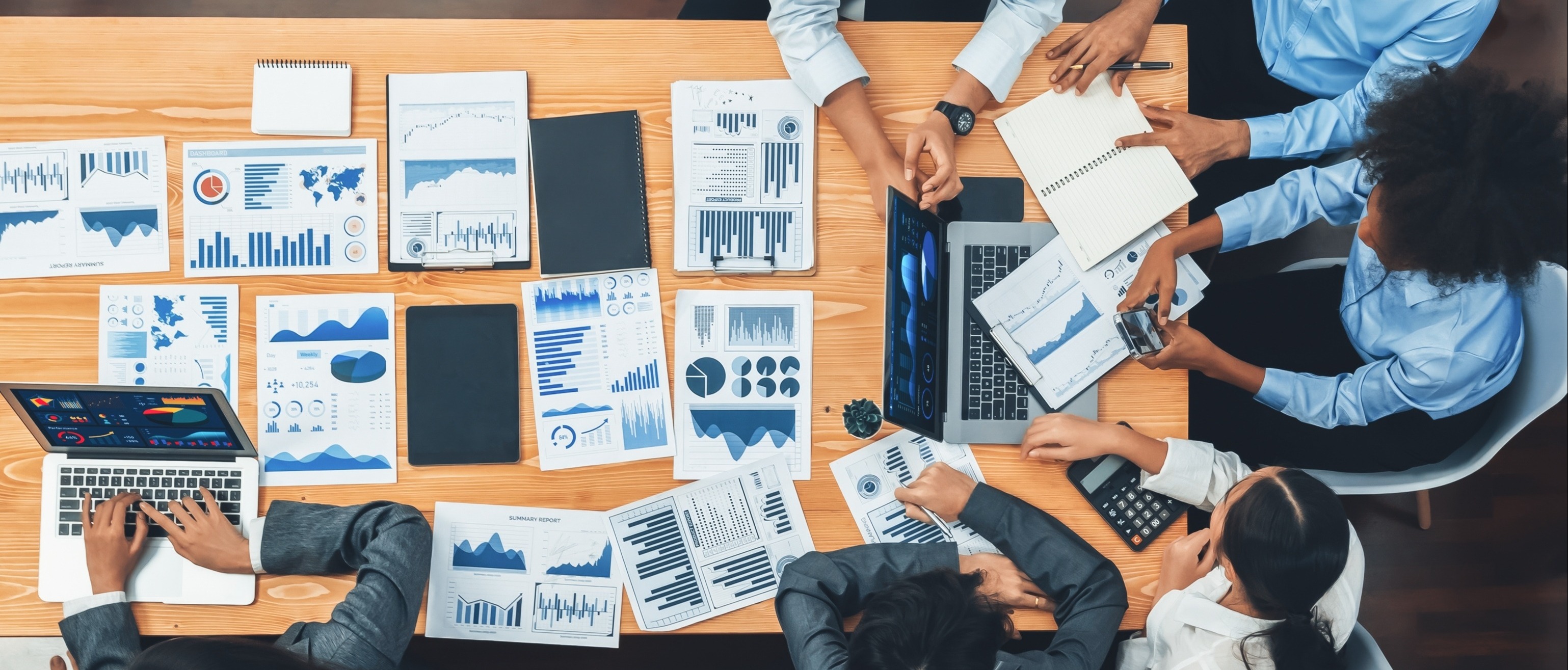 Overhead view of a diverse team collaborating around a table covered with graphs, charts, and laptops.